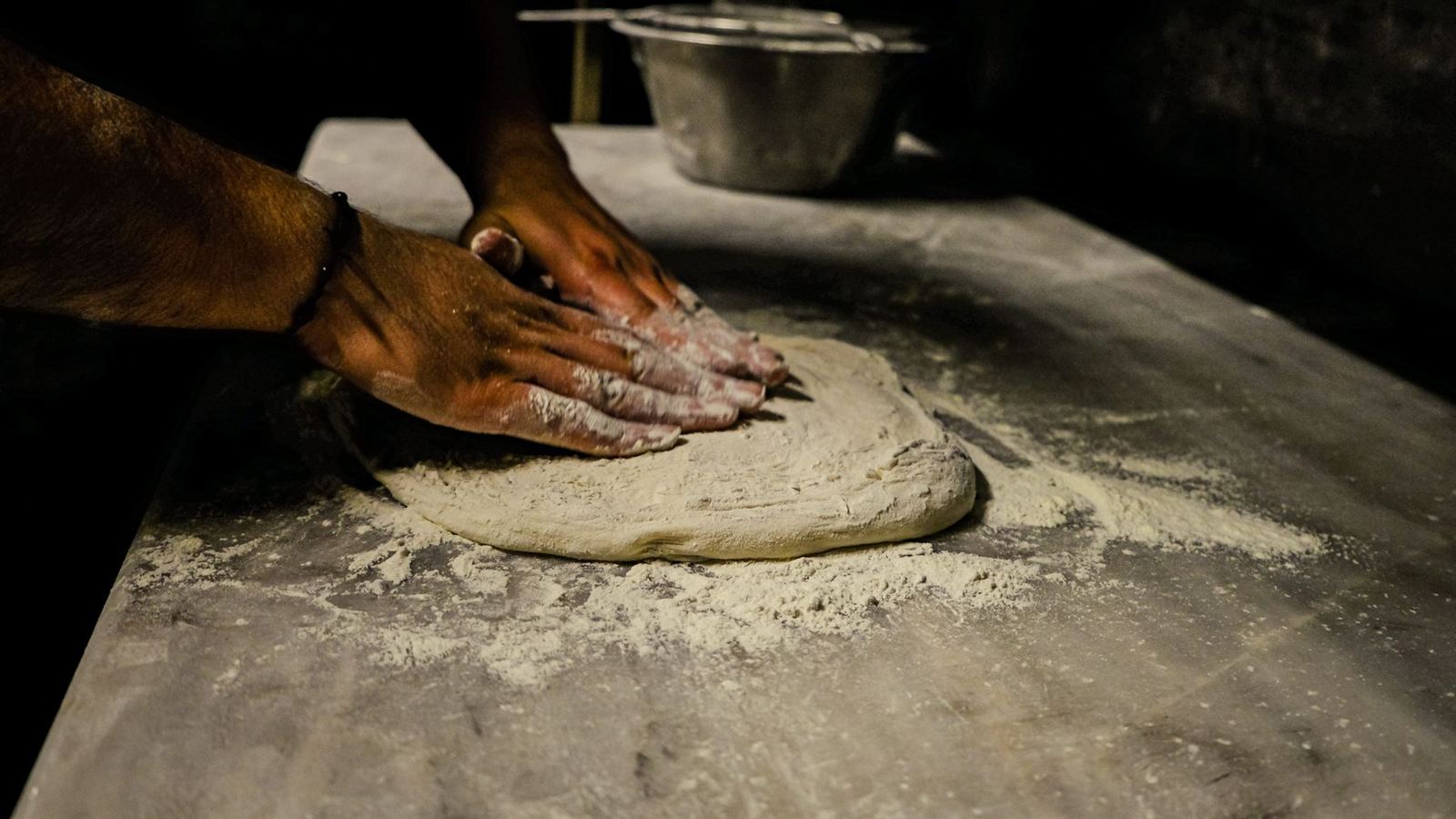 Des mains pétrissent une pâte à pizza sur un plan de travail fariné (photo d'illustration)