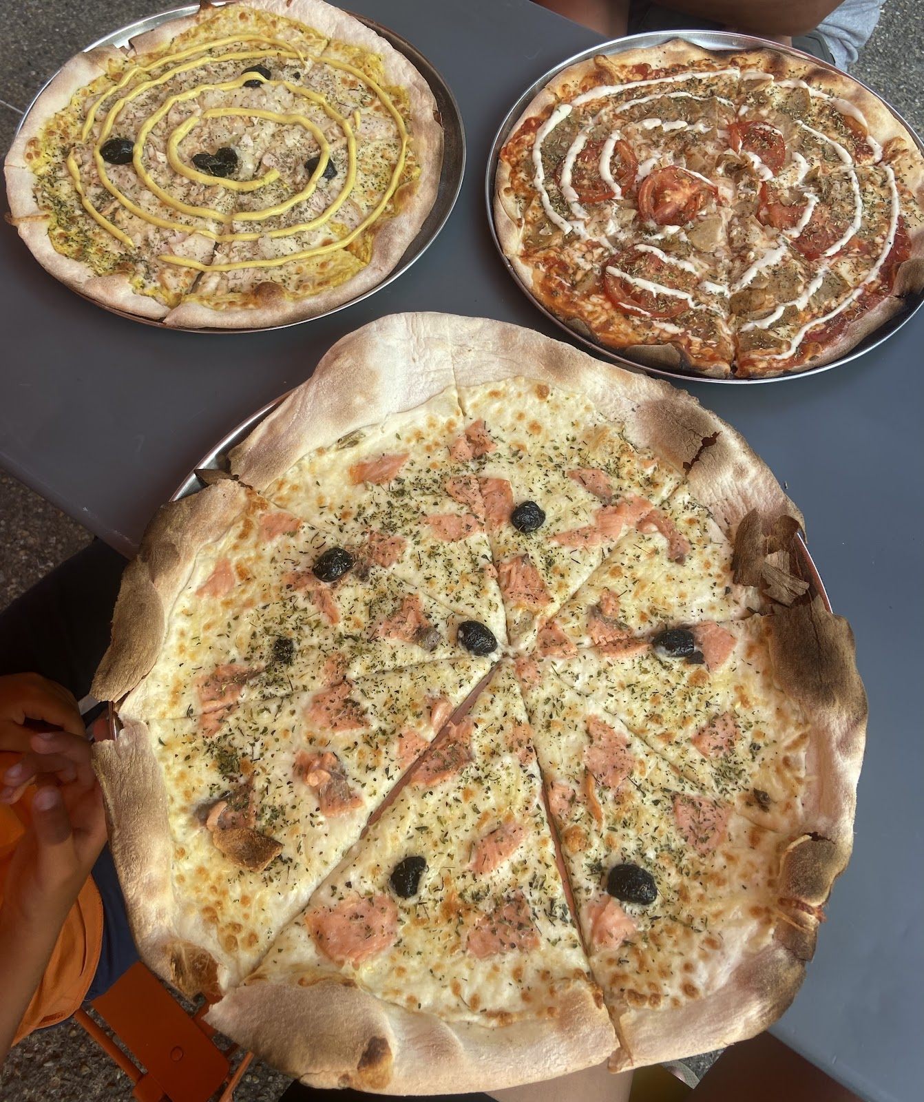 Trois pizzas sur une table : sauce blanche en spirale, moutarde en spirale, et une pizza au saumon